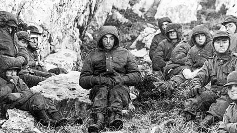 Silueta de un excombatiente de Malvinas con la bandera argentina de fondo, en un día nublado.