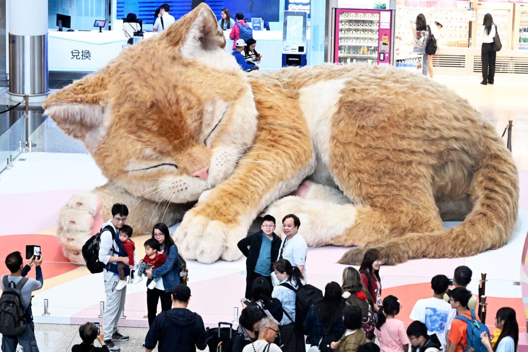 Viajeros toman fotografías frente a una gran escultura de un gato en el Aeropuerto Internacional de Hong Kong.
