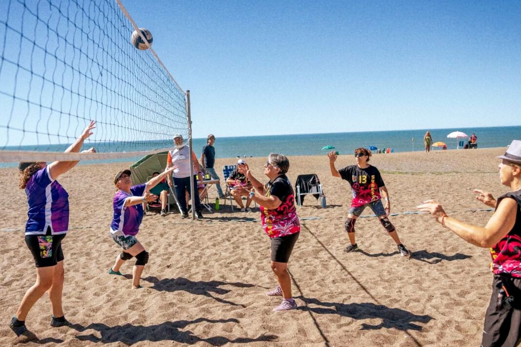 Grupo de adultos mayores jugando al newcom, atrapando y pasando una pelota en una cancha.