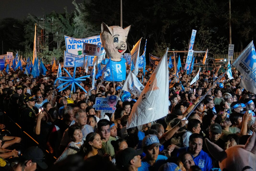 Multitud en un acto de cierre de campaña electoral en Lima, Perú, con banderas naranjas.