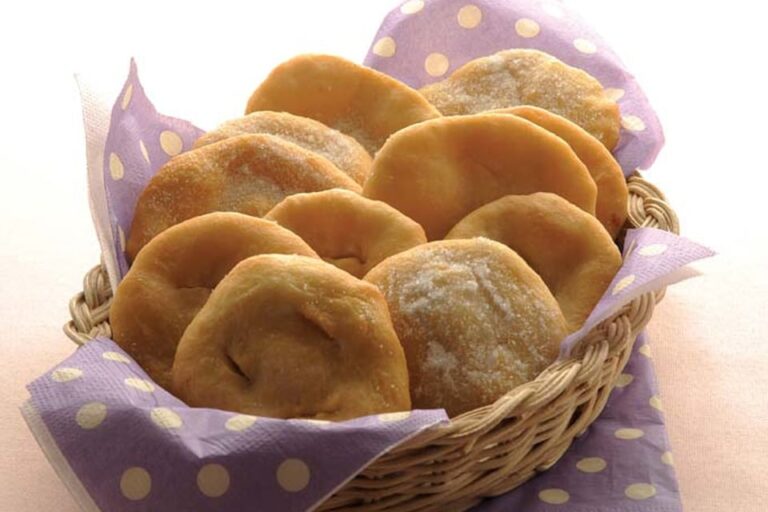 Tortas fritas criollas espolvoreadas con azúcar sobre una mesa rústica